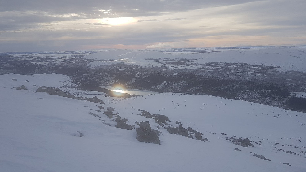 Fra toppen av Storhøa og mot sola som ble reflektert av isen på vannet