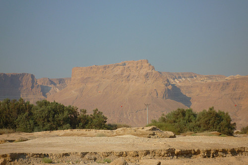 Masada-klippen i ørkenen i Judea, sørøst for Jerusalem. Ruinene etter Kong Herodes' palass kan skimtes oppe på platået, og "slangestien" sees i fjellsiden litt til venstre i bildet.