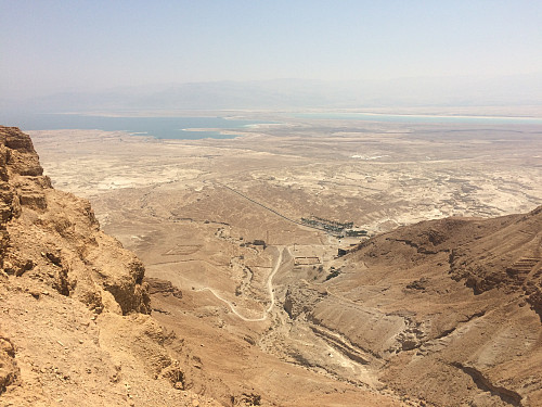 Utsikt fra sørspissen av Masada-platået. Det tørrlagte elveleiet er Metsada-elven der den løper mellom Masada og Mount Eliezer, bygningen med palmene omkring er turistsenteret, og sjøen i det fjerne er Dødehavet.