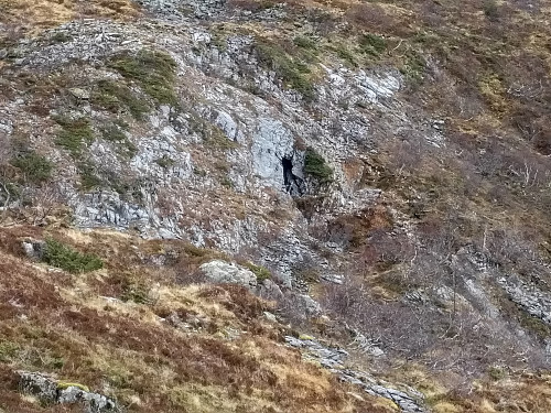 #8: Åpningen på grotte nummer 2 sett fra borte ved Trolldalsvatna. Stigen som fører ned i åpningen er såvidt synlig, og sees litt lettere dersom man forstørrer opp bildet.