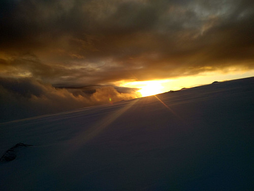 All of the sudden the low sun could be seen between the snow-capped mountain beneath, and the heavy clouds above.