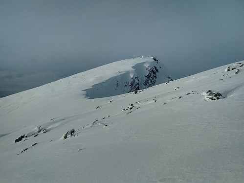 View of the main peak of Mount Smørbottind from a slightly lower secondary peak called the South Peak of Smørbottind. Note the snow shelves in the summit area, which may break off if you step onto them.