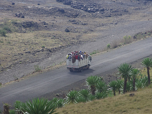 #64: A lorry loaded with goods, and then passengers on top of it; climbing the east side of Bwahit. The trail that we were following up to the Bwahit pass is located a little bit higher up in the mountain side. The road crosses over to the Chennek side of the mountain just south of the summit, as might be seen in images ##63 and 65.