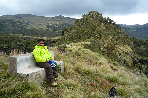 #1: My wife sitting on a concrete bench on the ridge of the Chennek Viewpoint. The main viewpoint is the little hill seen to the left of her. The ridge on which we're located extends north in a steplike fashion, thereby creating multiple viewpoints at different levels. Image captured the same afternoon, when I took my wife to the Chennek View Point for her to have a look at the view.
