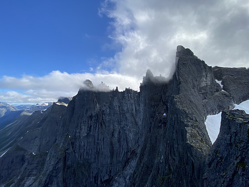 Image #18: View of vertical cliff called Trollveggen [i.e. "The Troll Wall"] as seen from Mount Nordre Trolltind. The larger peaks flanking the top of the cliff, are Store Trolltind [i.e. "Greater Troll Peak"], Brudgommen [i.e. "The Bridegroom"], Trollryggen ["The Troll's Back"], and Mount Breitinden [i.e. "The Broad Peak"]. The vertical cliff into the Rauma valley is about 1000 meters high, with the bottom of the valley being about 1700 meters below the peaks on top of the cliff.