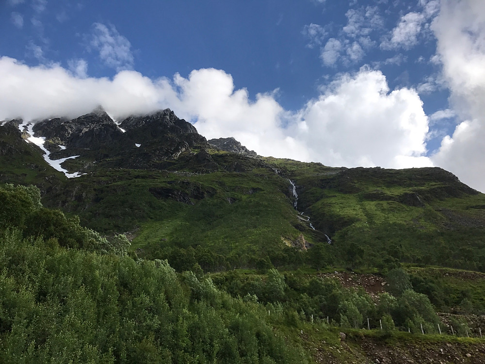 Nede ved bilen er det jo nesten sommervær! Stien går på venstre side av bekken opp til platået omtrent midt i bildet. Der krysses bekken og stien svinger langt ut til høyre før det fortsetter oppover. Snørenna som følges ligger skjult i skaret til høyre.