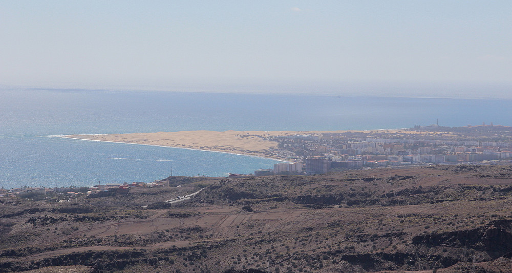 Syden: Utsikt fra toppen mot bl.a. sandynene Las Dunas, Playa del Inglés og Maspalomas. Motorveien GC-1 skimtes også et kort stykke i forgrunnen.