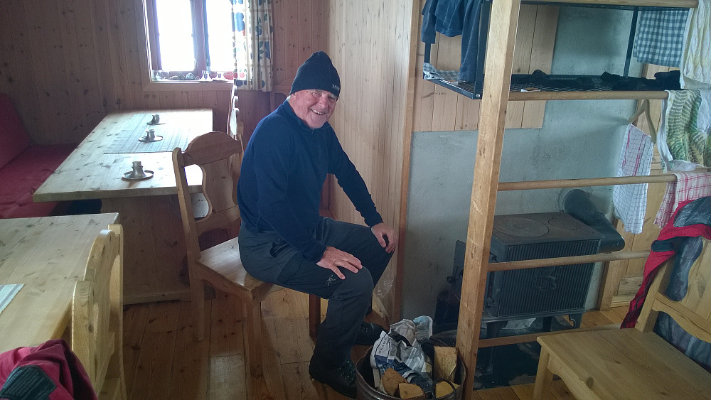 Knut Sverre varmer seg ved vedovnen i stua på Fonnabu, mens vi venter på opplett i været.