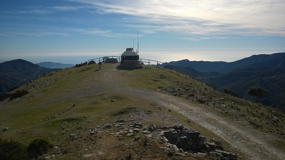 Ha, bildet ser forvrengt ut, men det er det ikke. Like ved toppen ligger et mystisk hus med antenne. Sittebenk ved gjerdet var det også, og et nedslitt skilt som skulle vise utsikten og navn på fjellene.