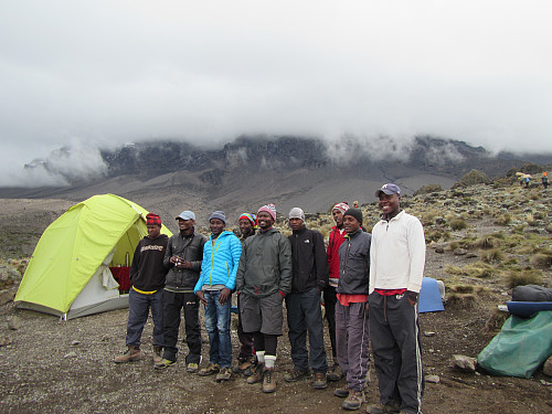 Hvor mange tanzaniere trengs det for å få to nordmenn til toppen av Kilimanjaro? Ni, to guider, kokk og seks bærere :) Kilimanjaro gjemmer seg i skyene