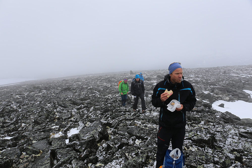 Jarle "nyter" en brødskive på toppen av Vestre Skardstind. Snøværet har lagt igjen glatte steiner på alle kanter.