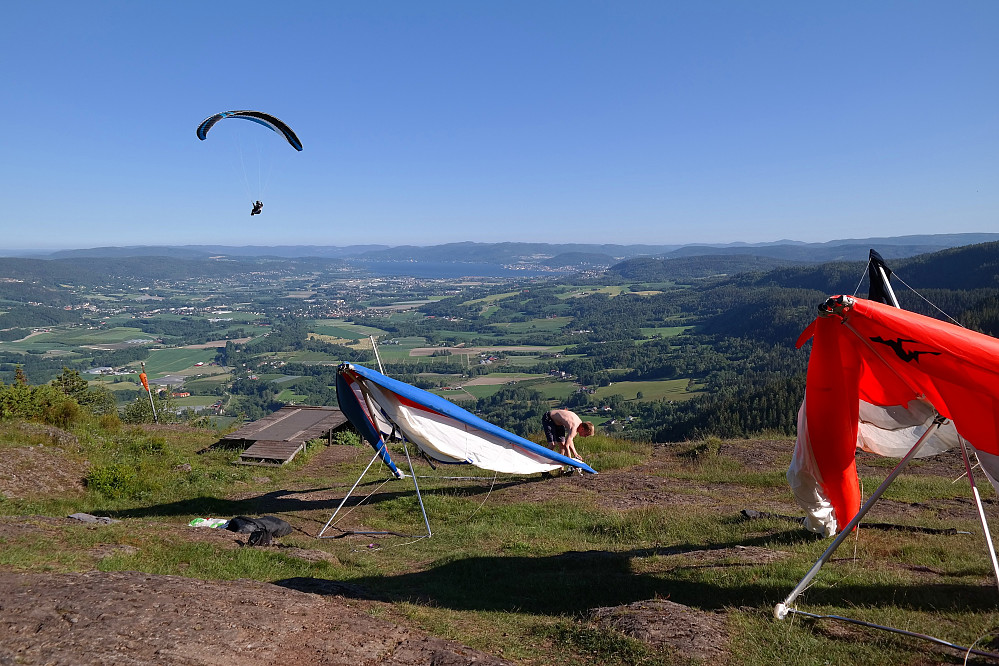 01.07.2015 - Ståle godt i gang med å montere sin hangglider. En kar i paraglider svever i bakgrunnen. Langt bak (over Ståles hangglider) ses Drammensfjorden.