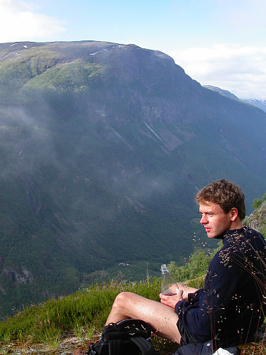 13.07.2003 - Johan Kristian tar en pust i bakken etter å ha gått stien opp Brendeteigen. Nede i dalen ses Vetti Gard, hvor vi startet turen til fots.