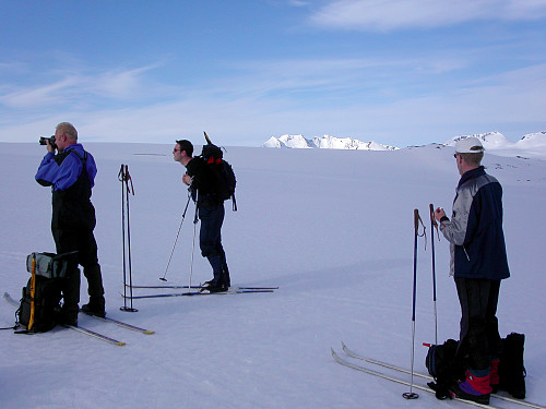 19.06.2005 - Erik, Roger og Erling nyter morgenen på Leirbrean mens sola fremdeles lå bak et skydekke. I bakgrunnen lyser derimot Hurrungane opp.