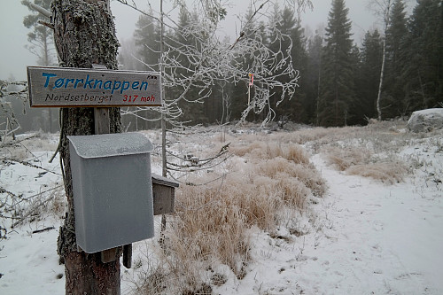 Få meter vest for høyeste punkt på Nordsetberget passerer stien. Her er det skilt og postkasse. Toppen kalles visst også Tørrknappen.