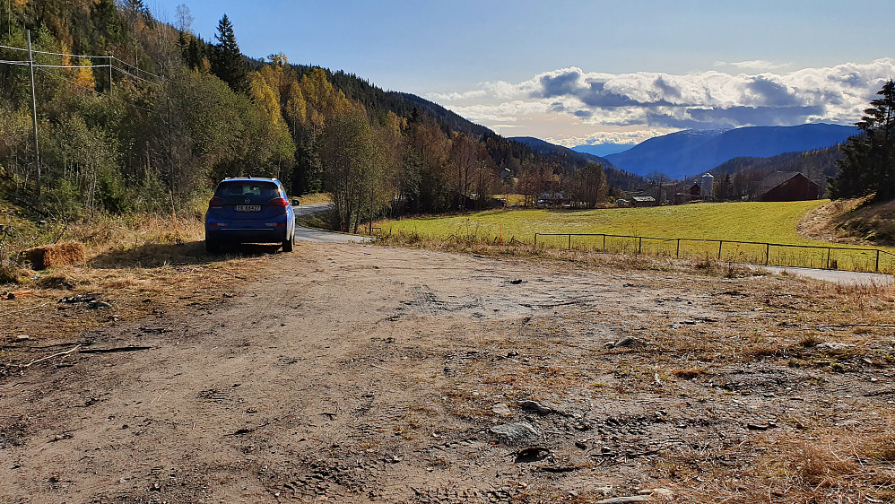 Parkering der kjerreveien startet ved fylkesvei 364, som ses til høyre for bilen. Gården Mellom Rue ses til høyre på andre siden av jordet.