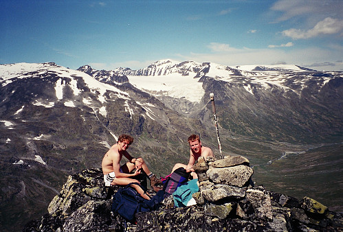 20.07.1996 - Johan Kristian og Hans Petter puster ut etter at 600 høydemeter var unnagjort opp nordryggen på Hellstuguhøe (2072). Nå gjenstår kun en slak liten stigning til Hellstuguhøe. Midt i bildet i bakgrunnen ses Galdhøpiggen (2469).