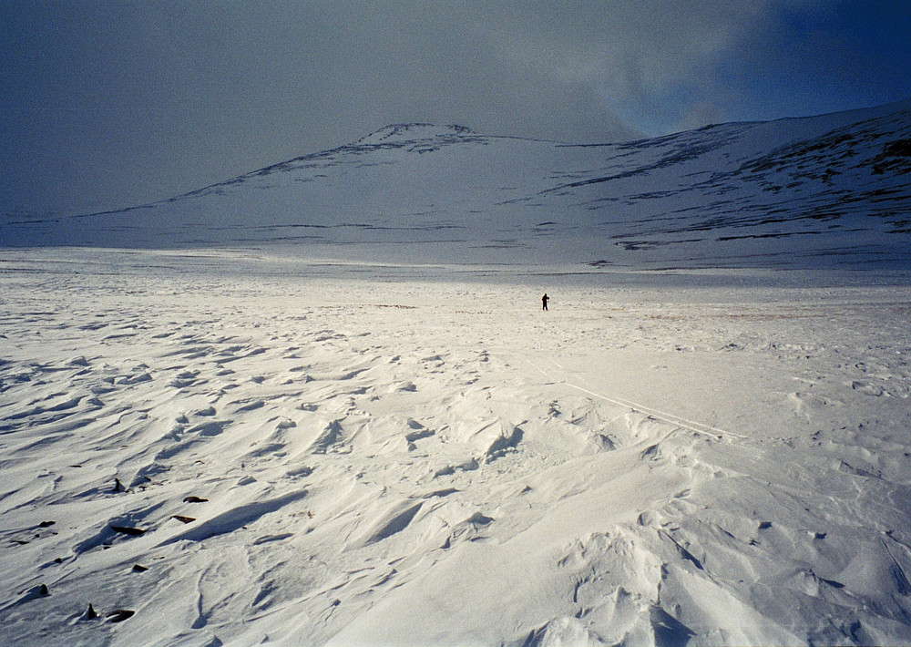 19.04.1997 - Retur fra Hindnubban. Fjellet bak, midt i bildet, er den østre enden på Austnubben (2049). Hans Petter kommer kjørende på hardt og ujevnt underlag på Hindflyin. Og en og annen stein titter opp av det tynne snølaget.
