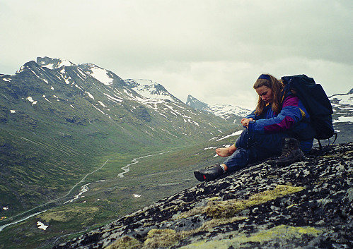 17.07.1998 - Grete vrir om våte sokker etter turen på Skagsnebb (2003). Det ble noe plumping og snø i skoa, samt regnvann på returen. Elva Leira og veien til Leirvassbu er nede til venstre.